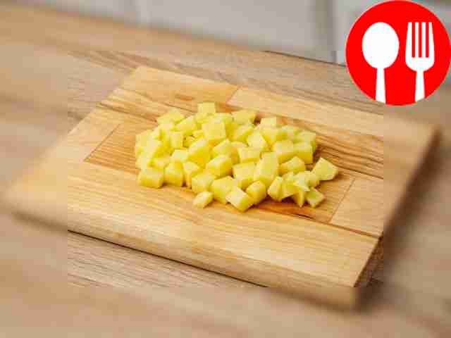 Нарежьте картофель кубиками на разделочной доске.